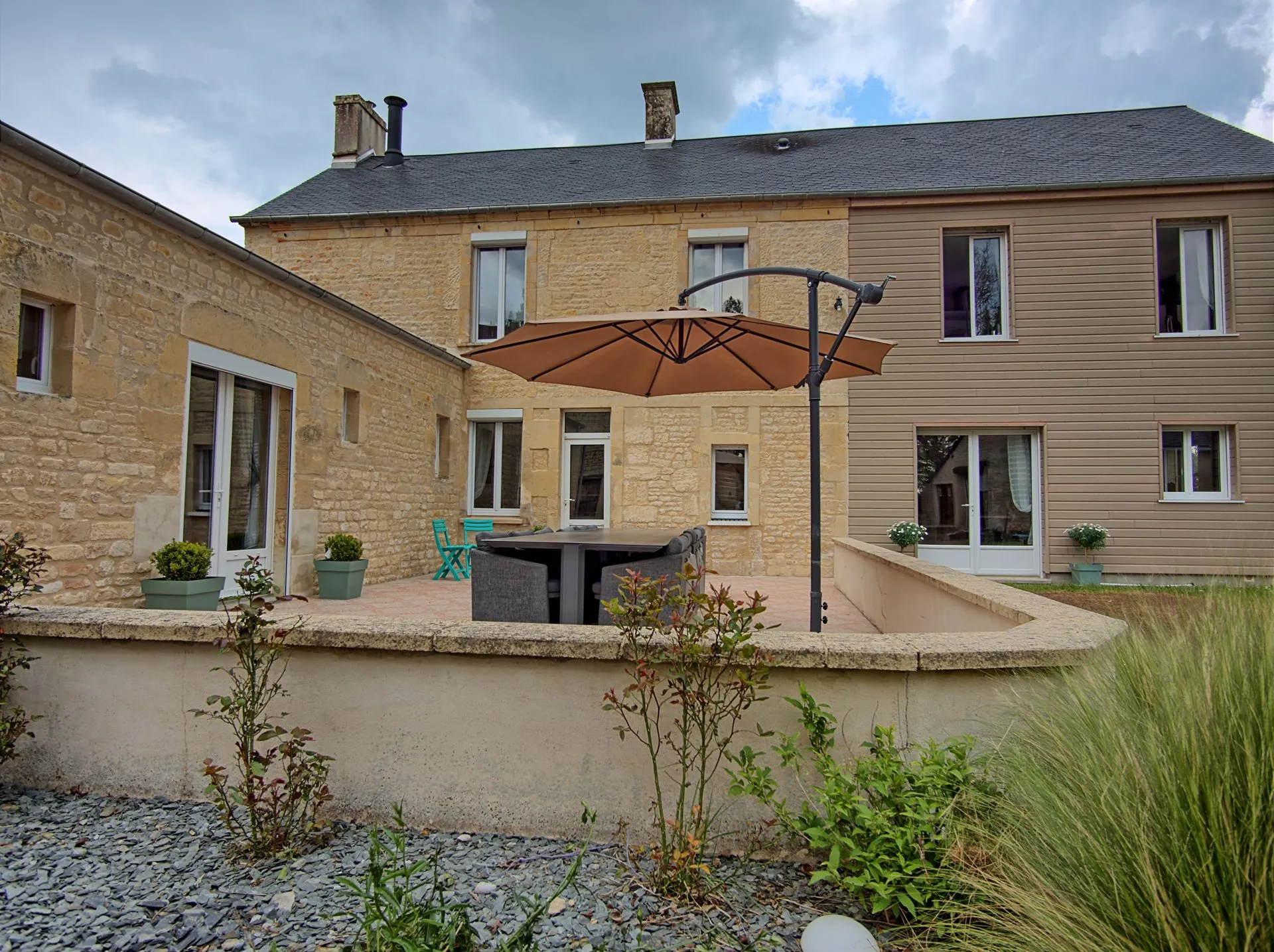 Terrasse avec parasol et salon de jardin, façade en pierre de Caen